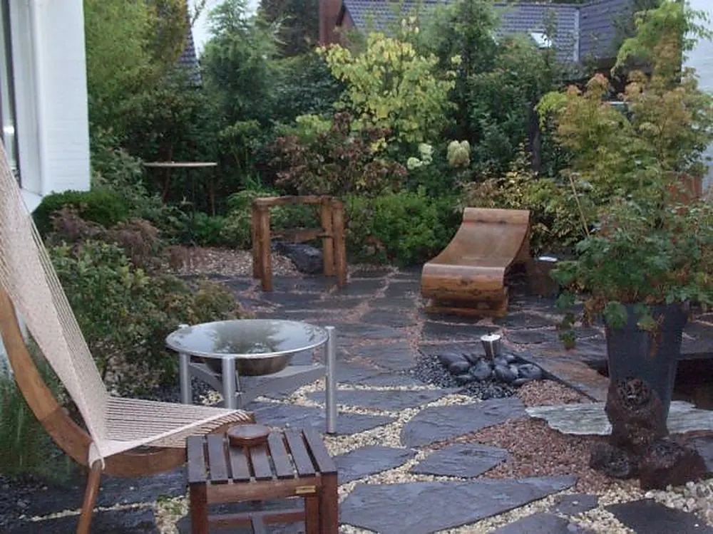 Garten-Lounge mit geschwungenem Holz-Sessel, Holztisch und Feuerschale