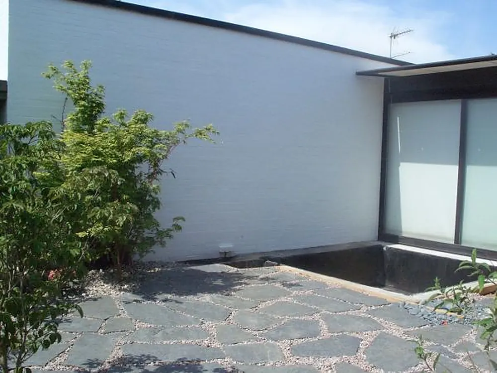 Innenhof mit weißer Wand, Wasserbecken und Steinpflaster mit Kiesfugen